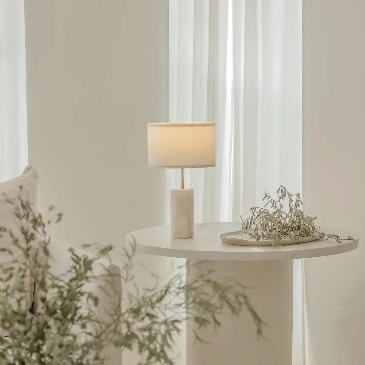 Lámpara de mesa de alabastro Barlet encendida con luz cálida sobre mesa redonda.